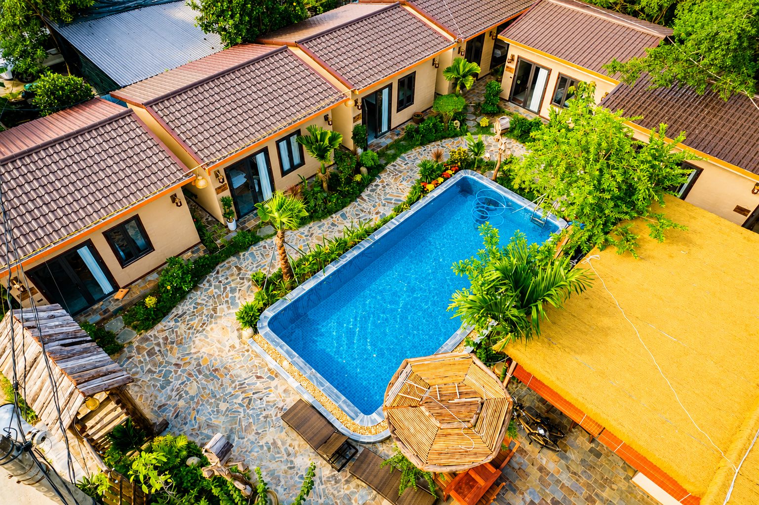 Bon's Homestay nhìn từ trên cao: dãy bungalow mái ngói ôm lấy bể bơi, sân lát đá và chòi tre